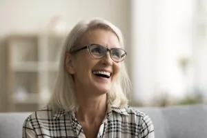 smiling older woman on a white couch, perfect new dental implants
