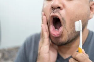 Man look in mirror touch cheek with hand and feels pain while brushing teeth due wisdom teeth