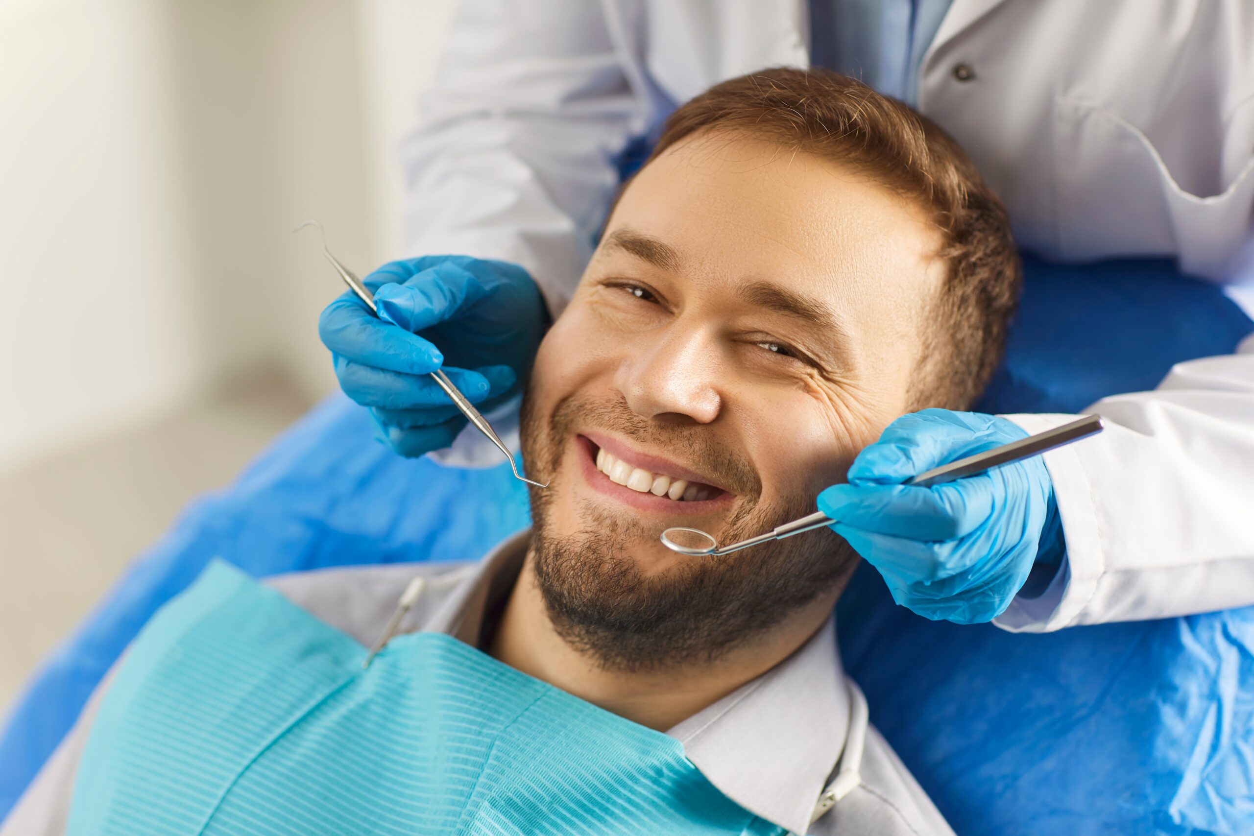 smiling man in dental chair, dentist in blue gloves